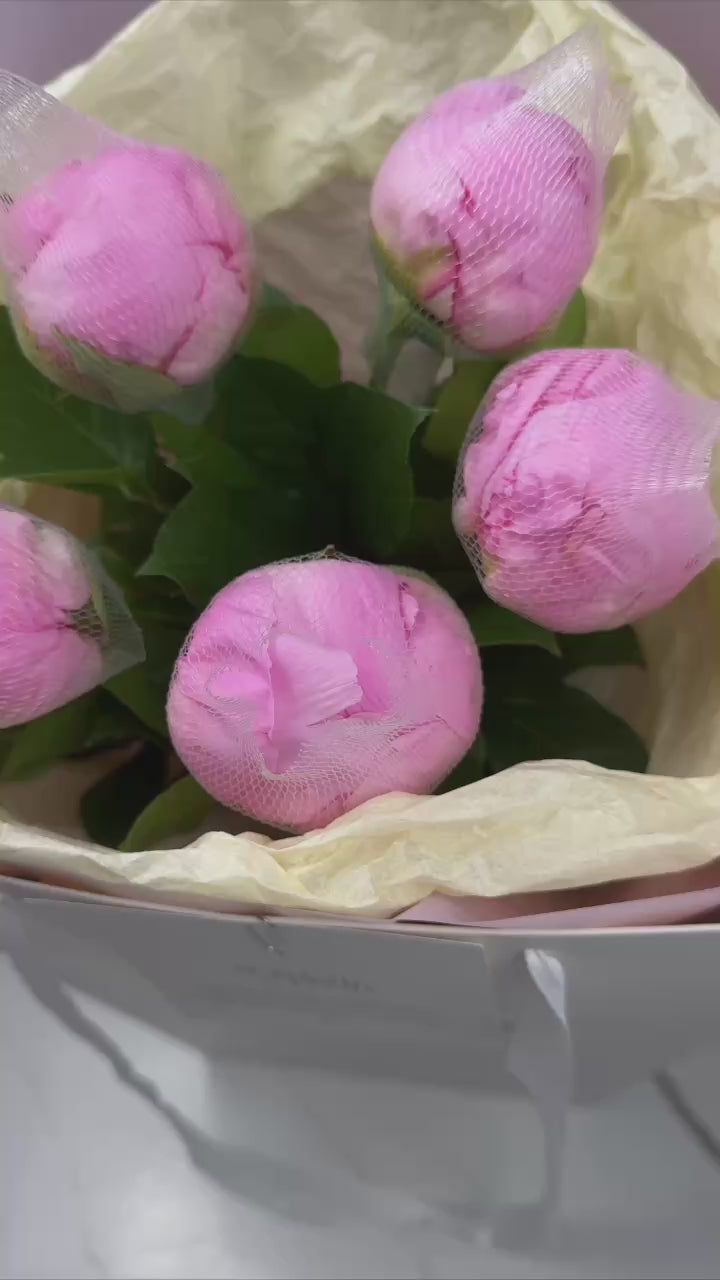 Close-up of pink peony buds wrapped in mesh netting in a luxury floral bouquet